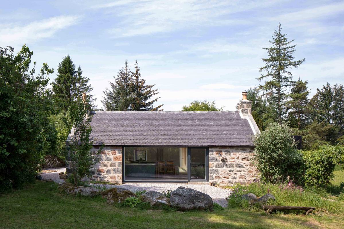 Granite cottage with full height glazing window surrounded by woodland and trees