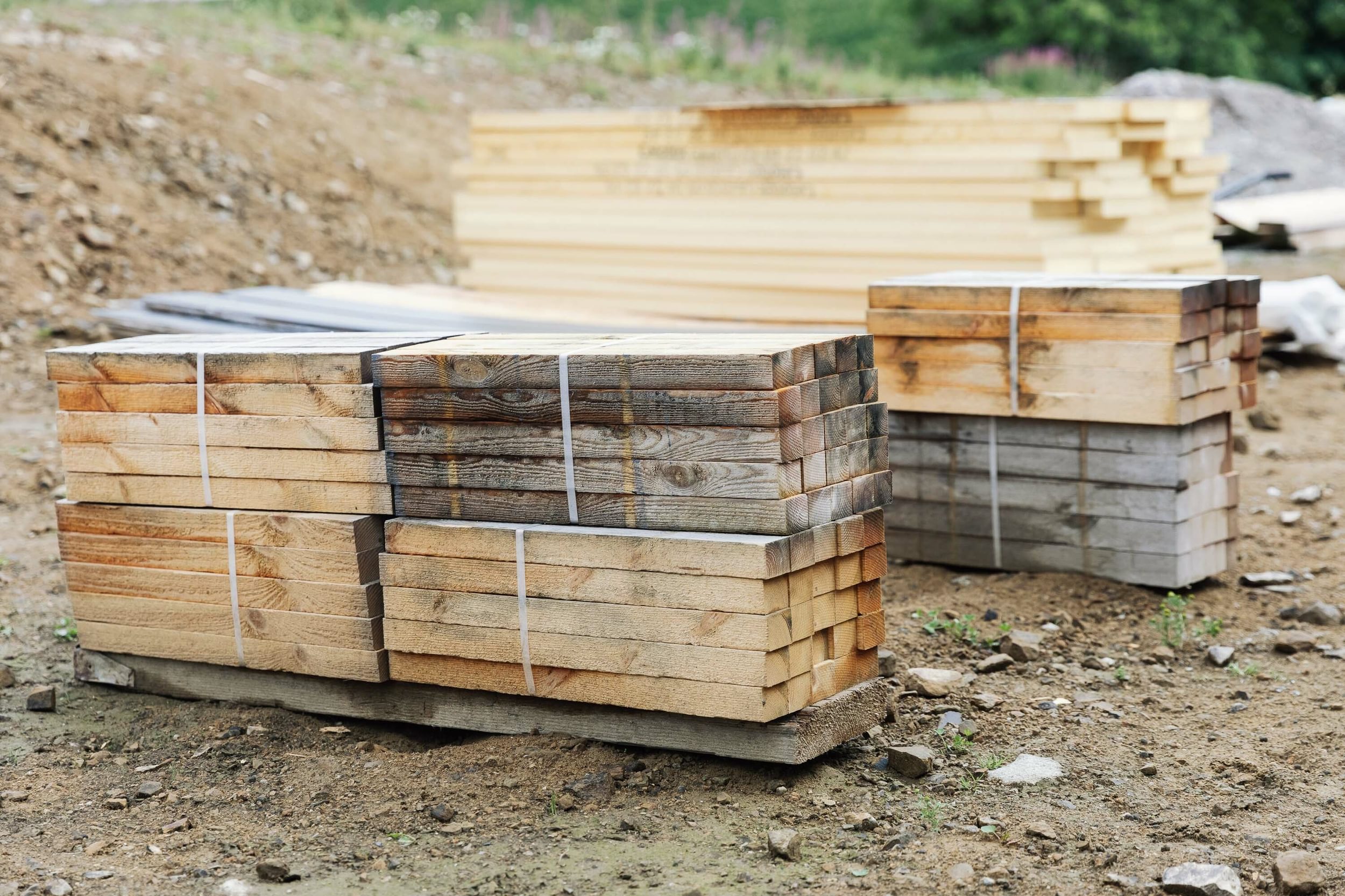 Timber stacked in piles and sitting on the ground at a new build construction site.