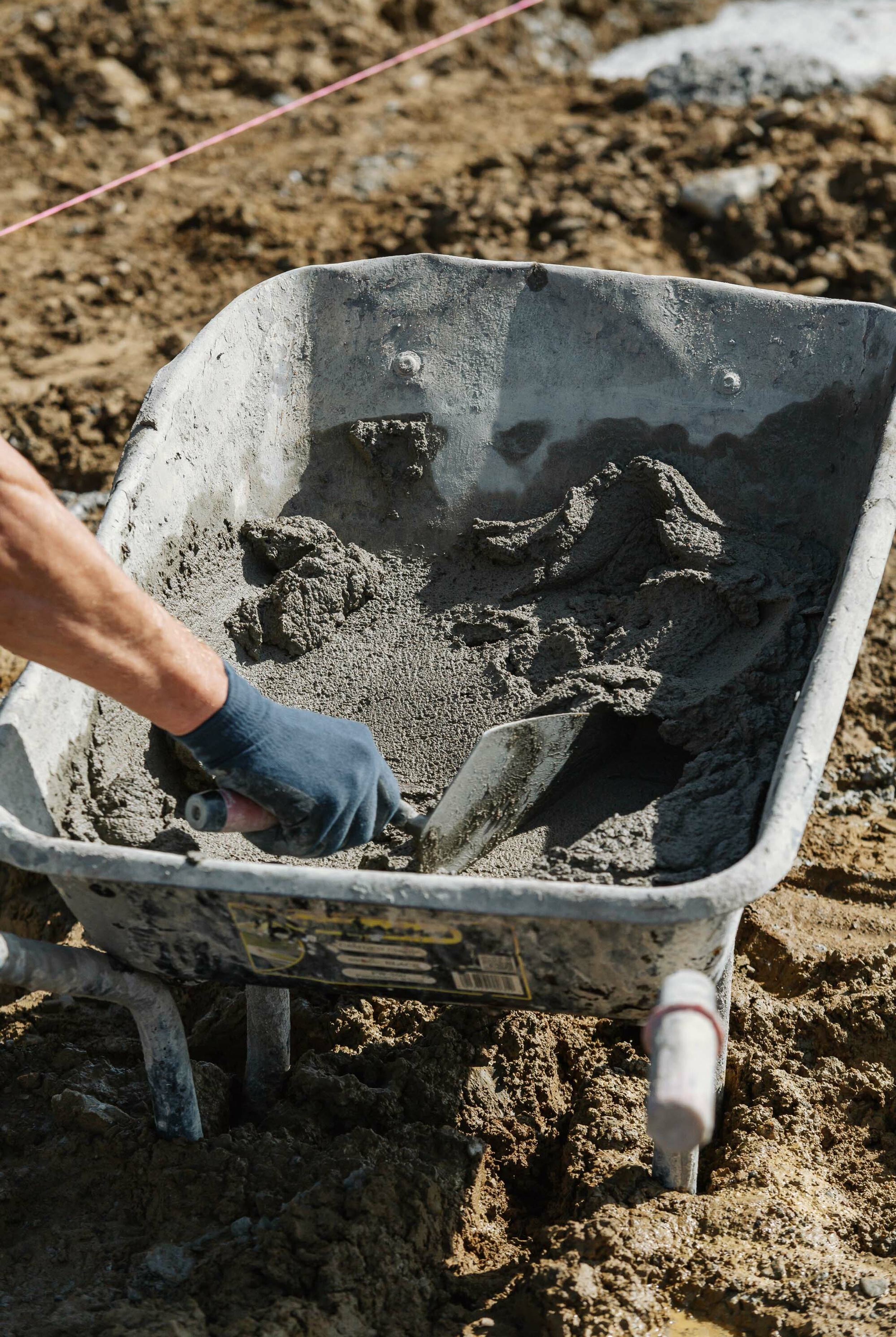 A builder dips his trowel into a wheelbarrow holding wet cement.