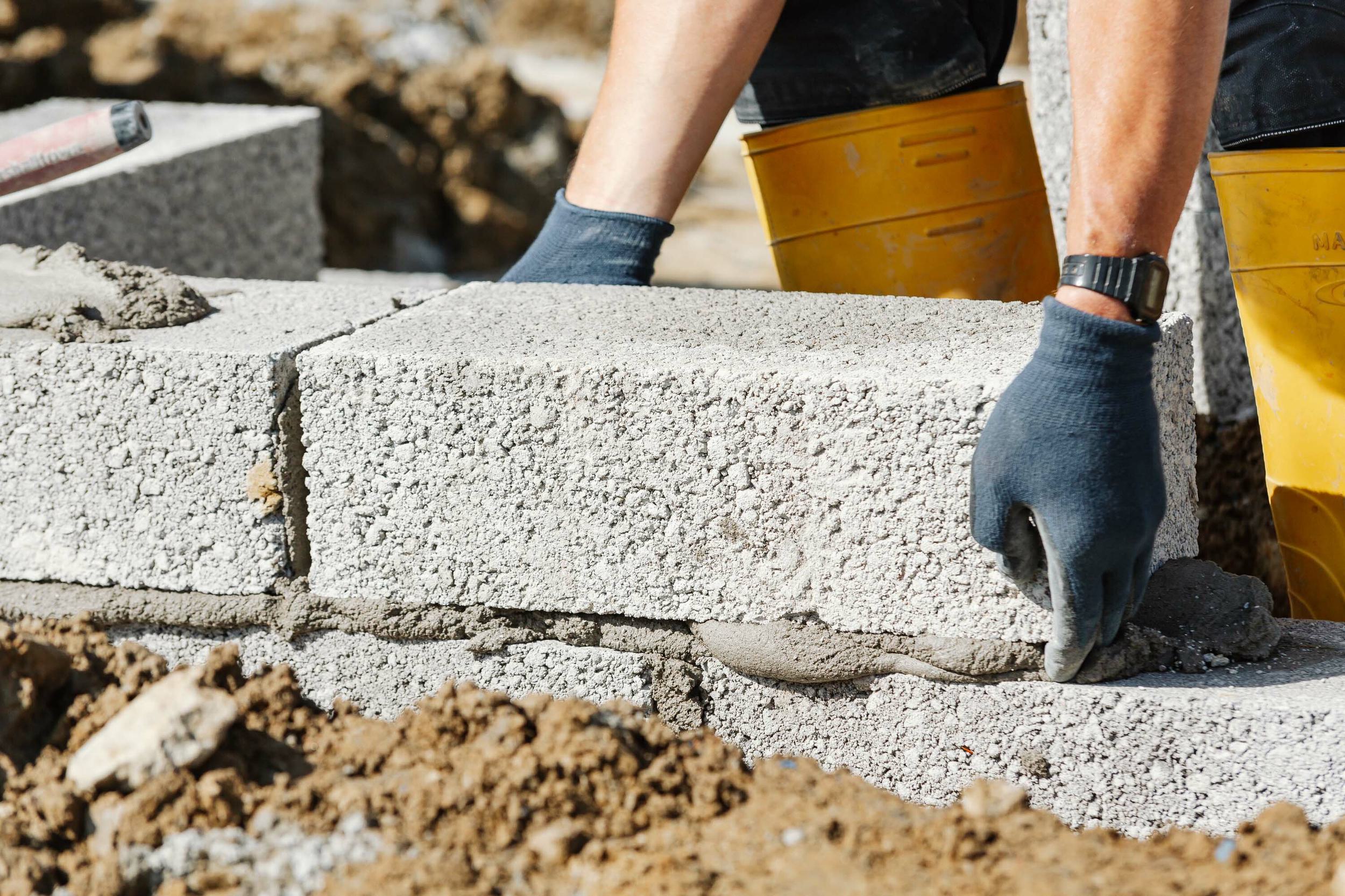 Close up of a concrete block being laid in wet cement to build the finished floor height of a new build home.